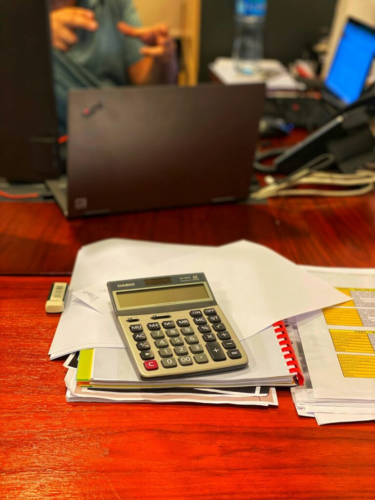A person reviews tax forms, receipts, and a calculator at a kitchen table.